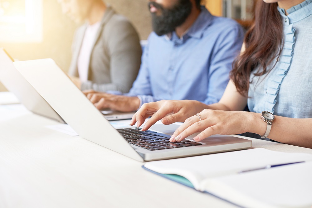 Close-up of business people sitting in a row and typing on laptop while sitting at office desk